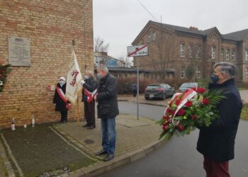 Kwiaty i znicze pod tablicą