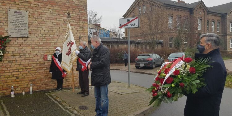 Kwiaty i znicze pod tablicą